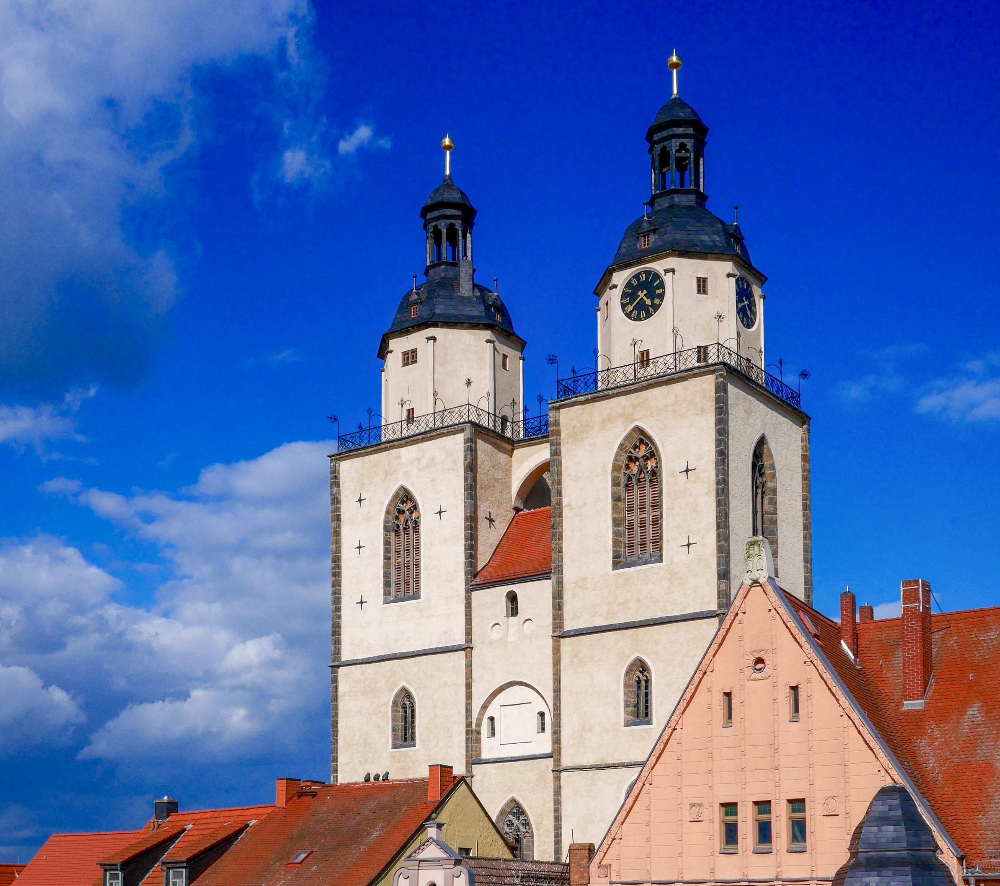 Die Wittenberger Stadtkirche St. Marien erhebt sich vor blauem Himmel hinter den Häusern am Markt